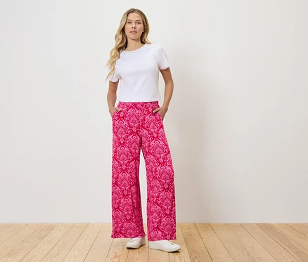 Frau steht mit Händen in den Taschen einer pinkfarbenen Hose mit Muster.