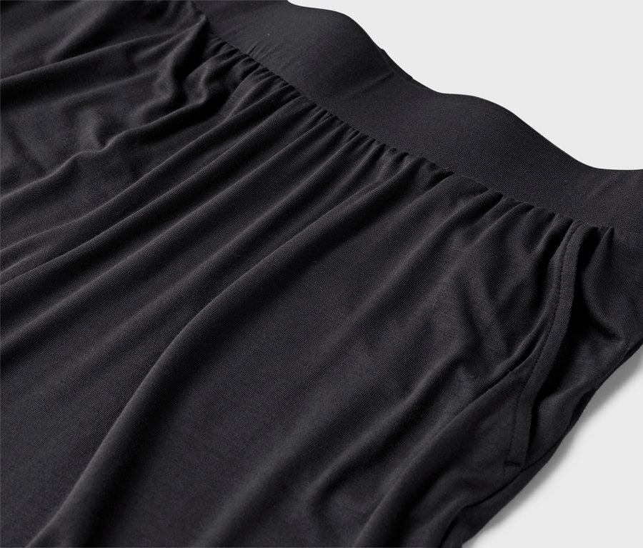 Detailaufnahme einer schwarzen Hose mit elastischem Bund und Taschen auf hellgrauem Hintergrund.