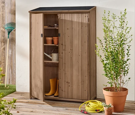 Ein offener Holzschrank steht draußen mit Gartengeräten, Töpfen, Gummistiefeln und einer Gießkanne im Inneren.