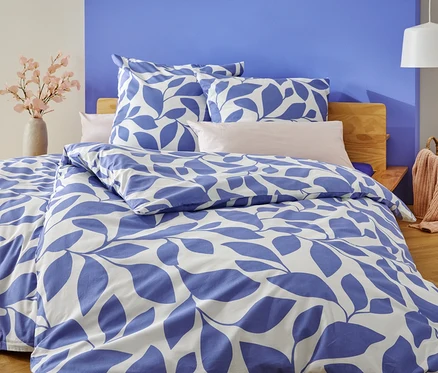 Ein Bett mit blau-weißer Blätterbettwäsche steht vor einer blau und weiß gestrichenen Wand.