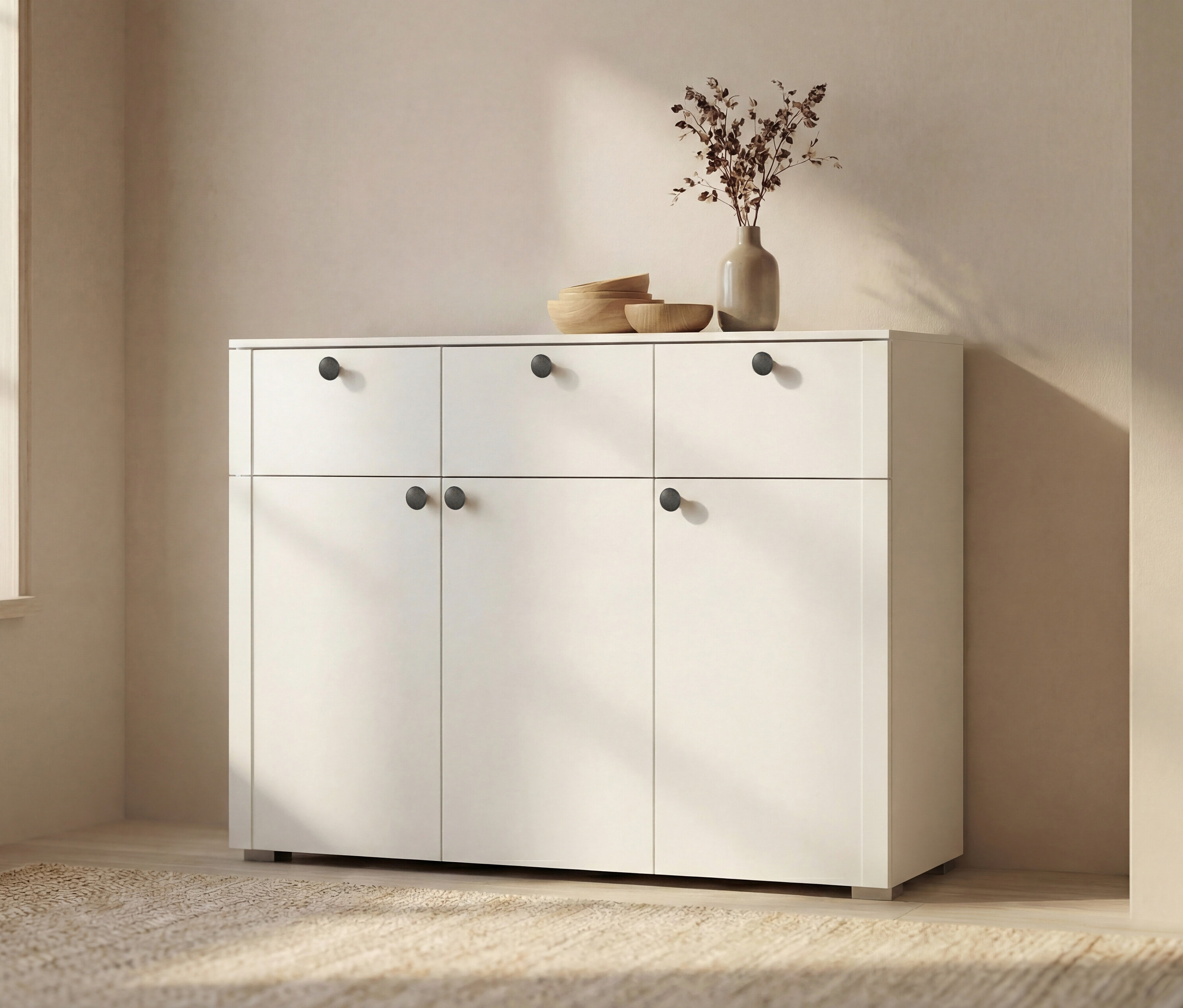 Weißes Sideboard mit sechs Schubladen und Türen, darauf eine Vase mit getrockneten Blumen und Holzschalen.