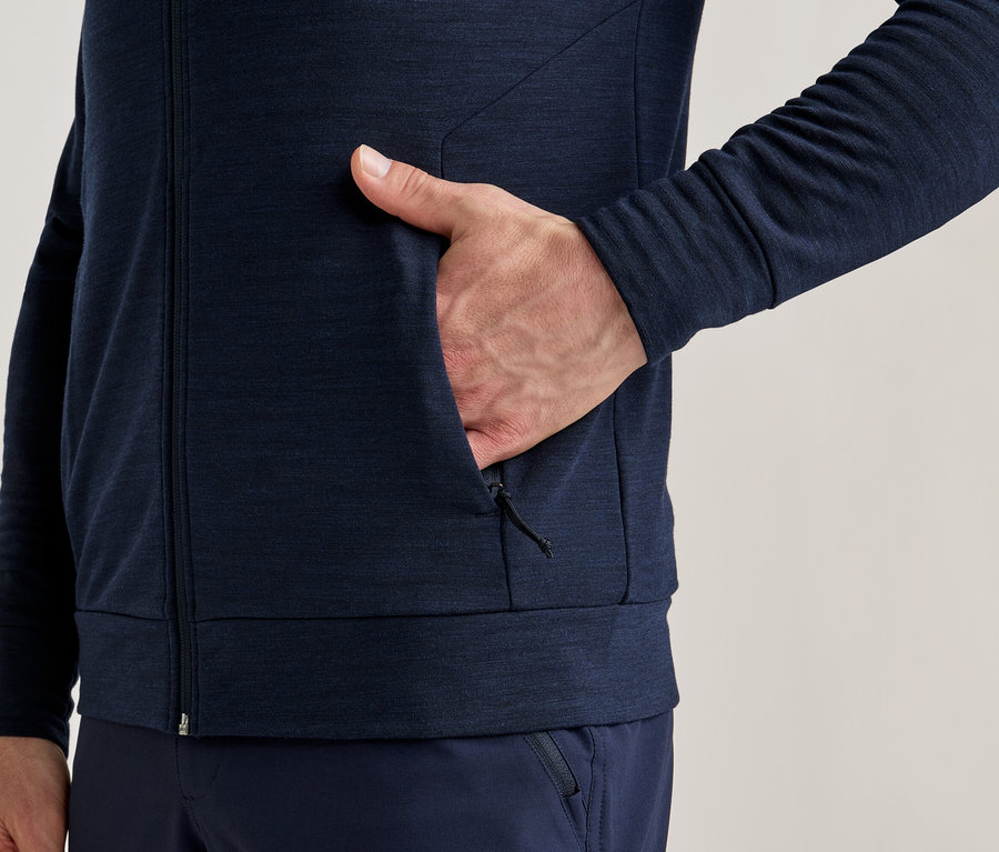 Nahaufnahme einer Person in marineblauer Jacke mit Reißverschluss und Hand in der Tasche.