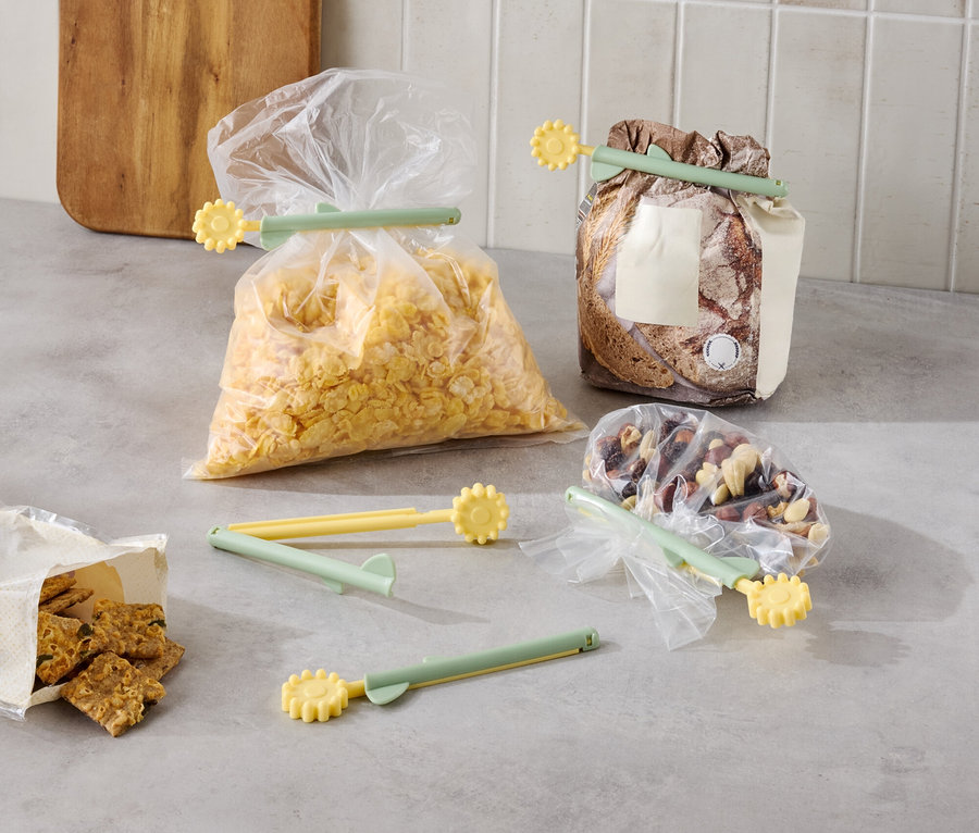 Verschiedene Lebensmittel sind in Tüten mit gelb-grünen Verschlussclips auf einer Küchentheke verpackt.