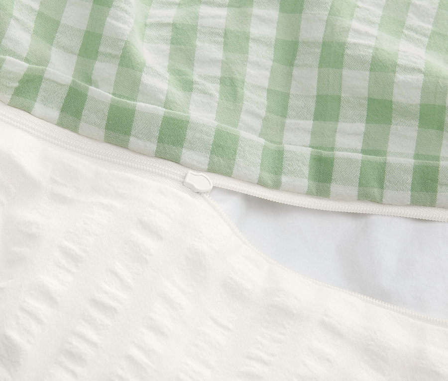 Nahaufnahme eines teilweise geöffneten Bettbezugs mit Reißverschluss, Oberseite grün-weiß kariert, Unterseite weiß mit Textur.