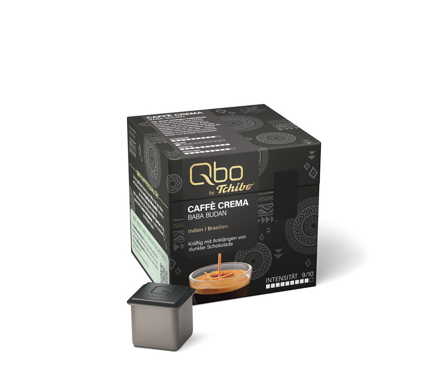 Schwarze Qbo by Tchibo Caffè Crema Baba Budan Kaffeekapselpackung mit Herkunftsangaben Indien und Brasilien, Geschmacksnoten von dunkler Schokolade und Intensität 9/10. Davor liegt eine einzelne Kapsel und ein Glas mit Kaffee und Crema.