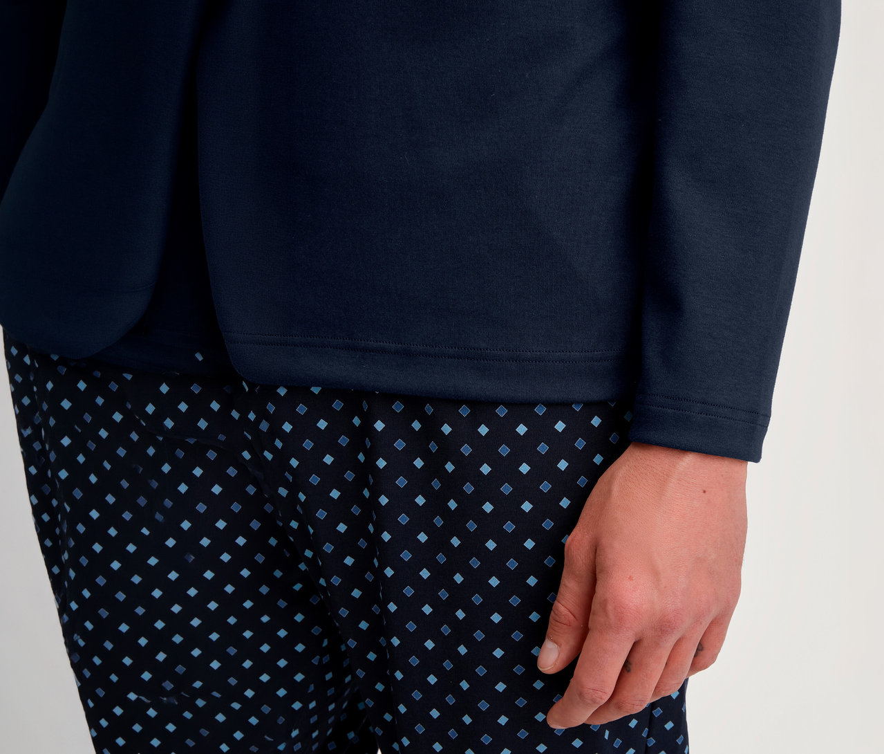 Nahaufnahme einer Person in einem marineblauen Langarmshirt und einer dunkelblauen Hose mit hellblauem Rautenmuster. Eine Hand ruht am Bein.