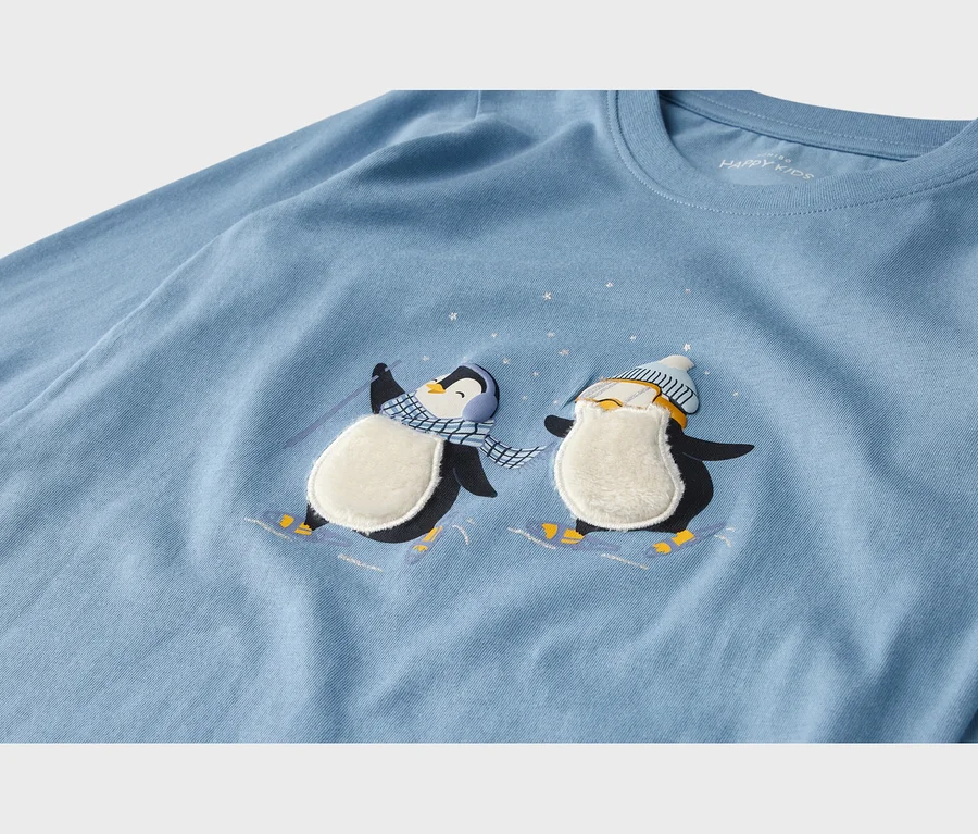Hellblaues T-Shirt mit zwei Ski fahrenden Pinguinen. Einer trägt Ohrenschützer und Schal, der andere Mütze und Skibrille. Ihre Bäuche sind flauschig.