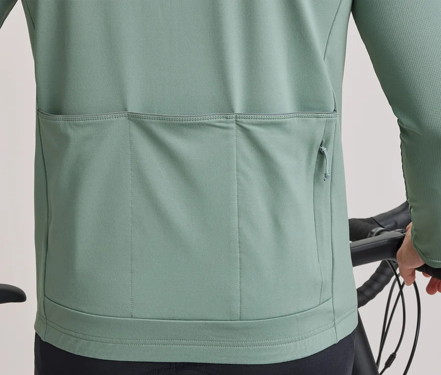 Rücken einer Person in hellgrünem, langärmeligem Radtrikot mit drei Rückentaschen, eine mit Reißverschluss, die einen Fahrradlenker hält.