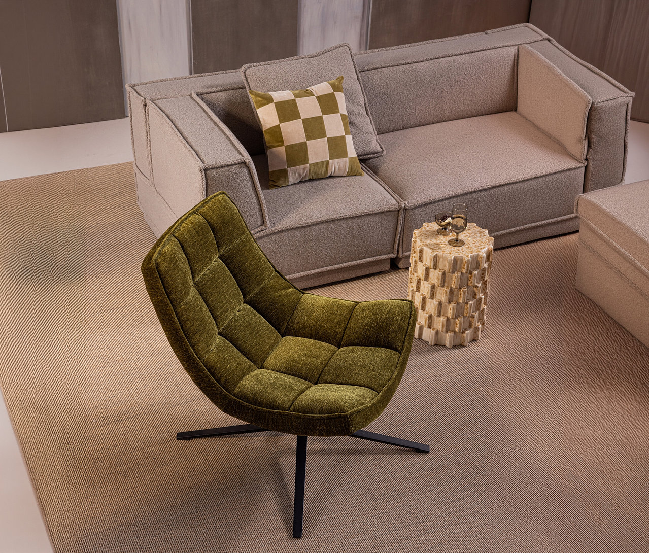 Grüner, gesteppter WOOOD Drehsessel »Maudi« vor einer hellgrauen modularen Couch mit kariertem Kissen und beigem Beistelltisch mit Gläsern.