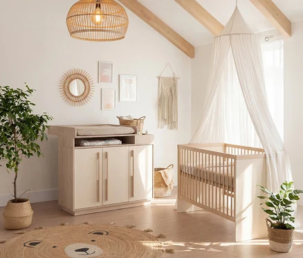 Babyzimmer mit hellem Wickeltisch, Gitterbett mit Baldachin, Pflanzen und einem Bären-Teppich auf dem Holzboden.