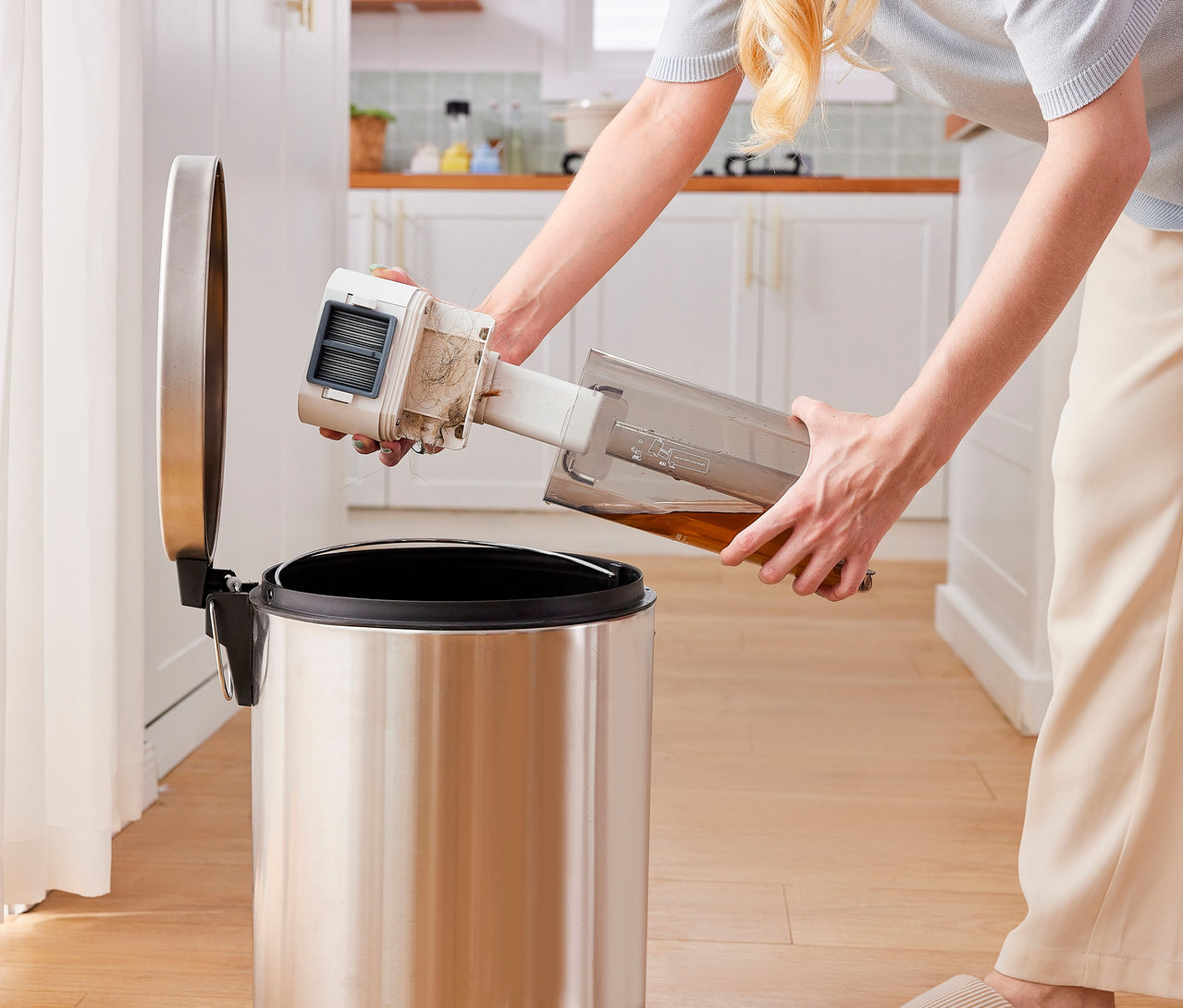 Eine Person leert den Schmutzwassertank und den Filter des Tineco 2-in-1-Nass-Trockensaugers »Y2 Plus« in einen Mùlleimer aus Edelstahl. Der Tank enthält braune Flüssigkeit, der Filter ist verschmutzt.