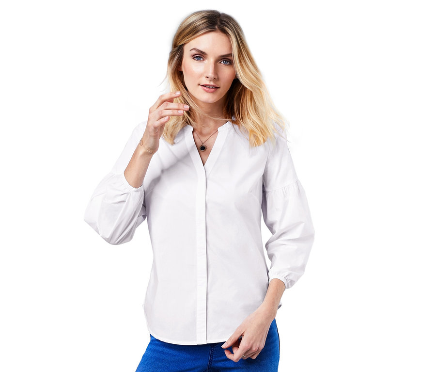 Frau posiert in Bluse mit Ballonärmeln und blauen Jeans.