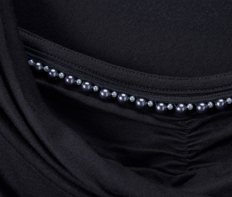 Detailansicht eines schwarzen Shirt mit Wasserfallausschnitt, verziert mit Perlen.