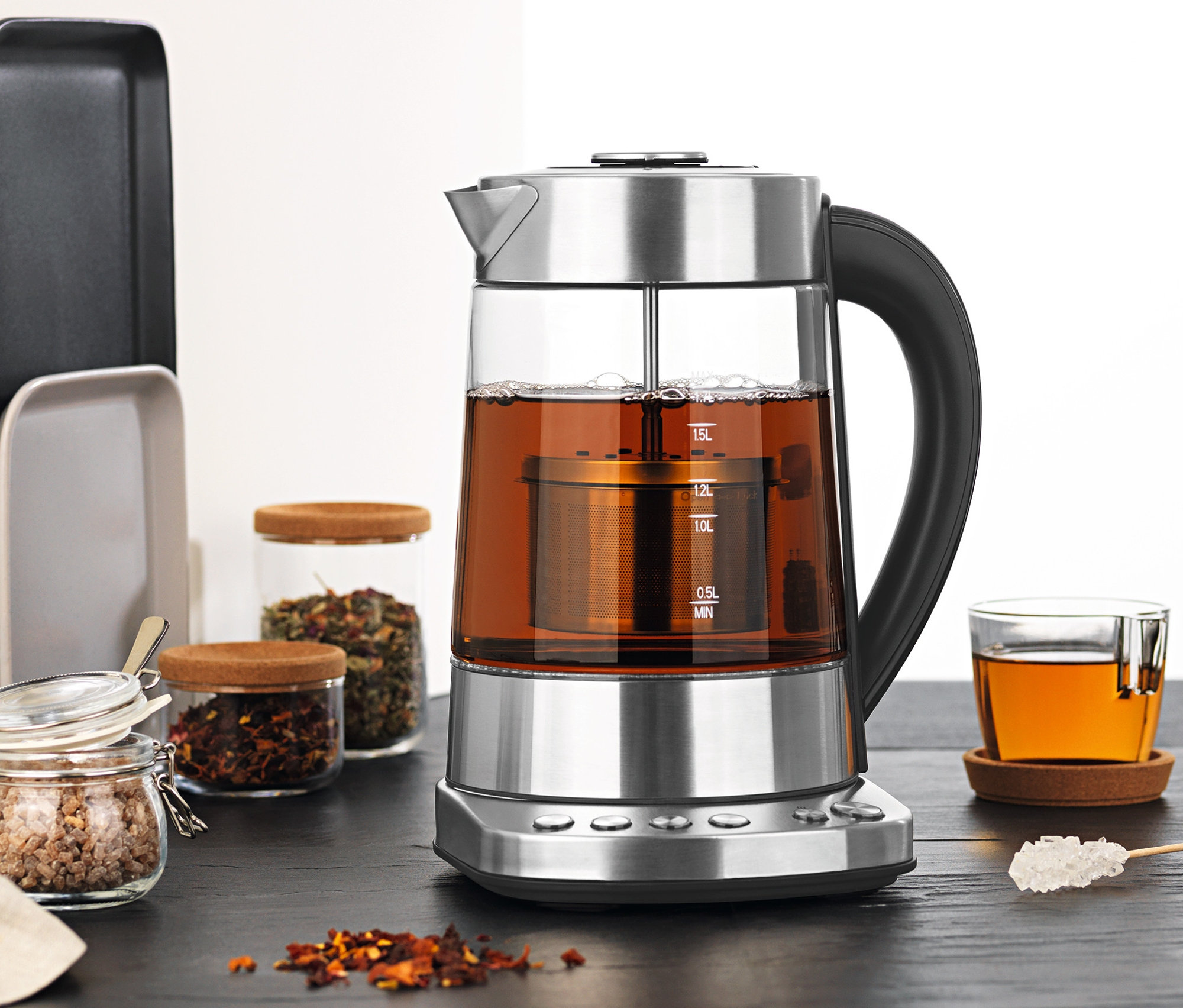 Ein Tee- und Wasserkocher mit 1,7-l-Glaskanne und Teesieb steht neben einem Glas Tee und Teegläsern.