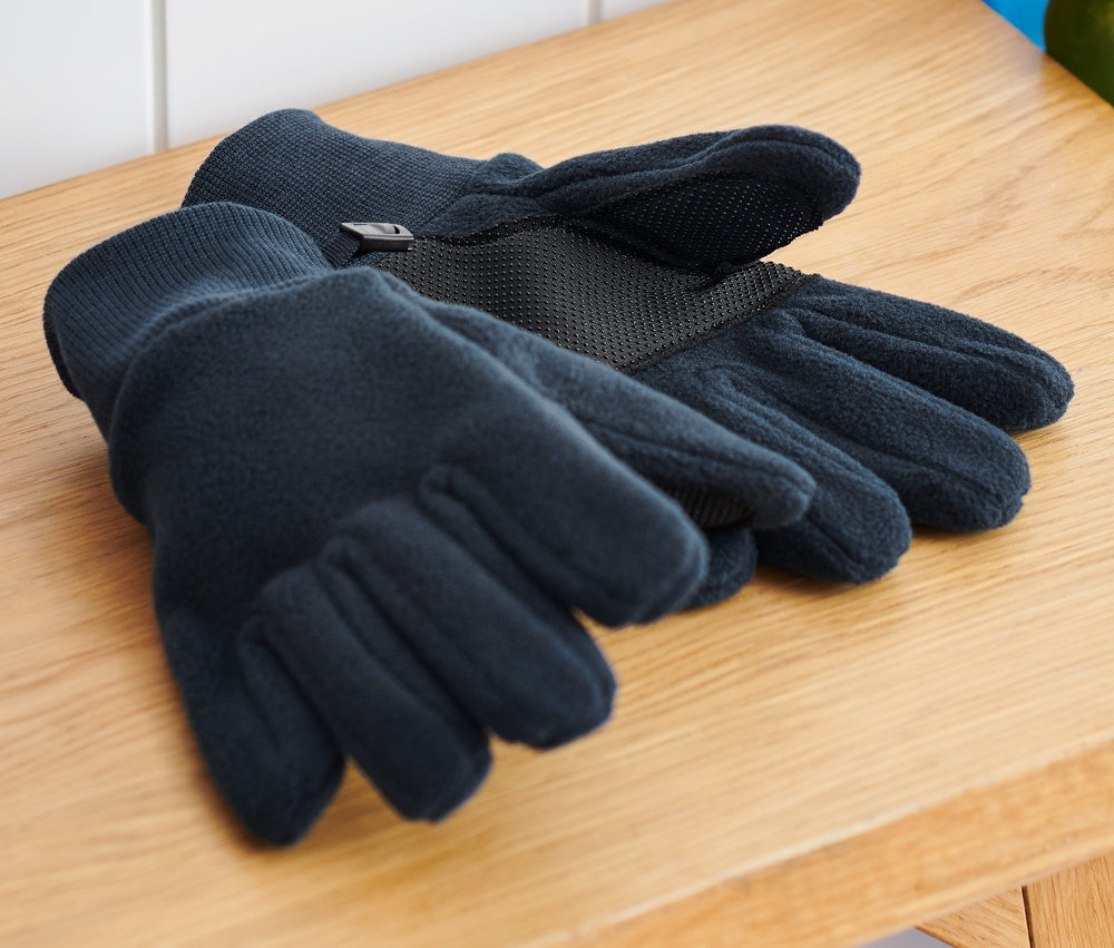 Kinder-Fleecehandschuhe liegen auf einer Holzbank neben einem Rucksack und einem Skateboard.