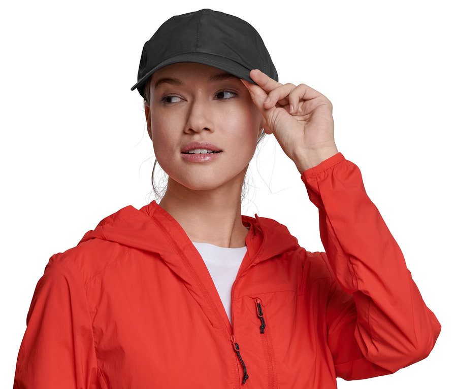 Frau berührt den Schirm einer Allwetter-Kappe. Sie trägt eine rote Jacke.