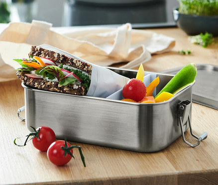 Eine To-go-Lunchbox mit einem Sandwich und geschnittenem Gemüse ist zu sehen.