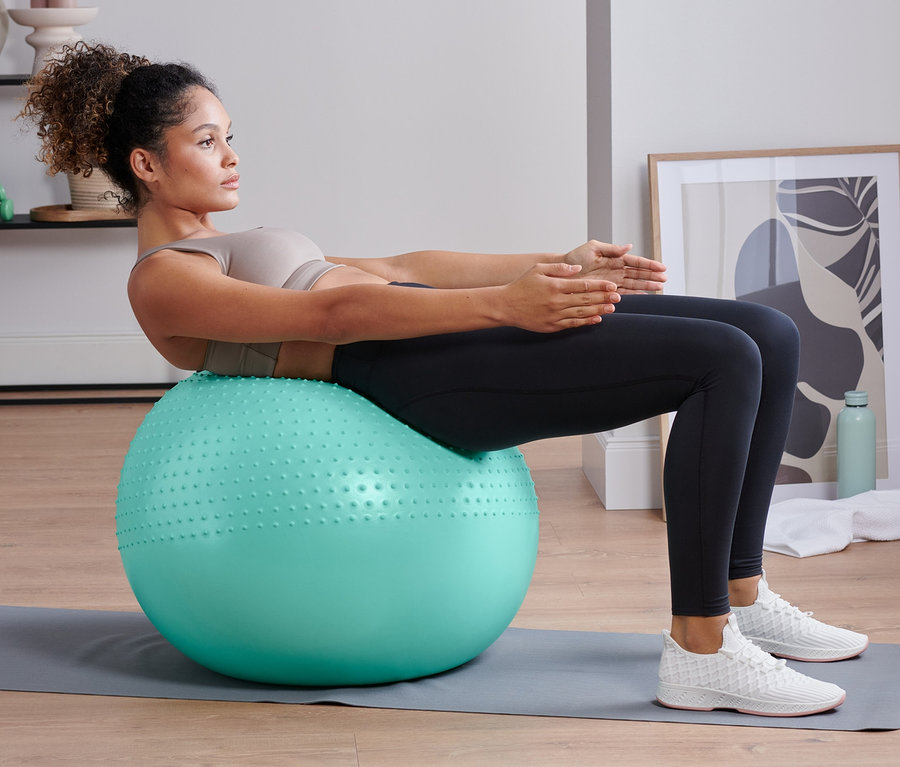 Frau macht Sit-ups auf einem Gymnastikball.
