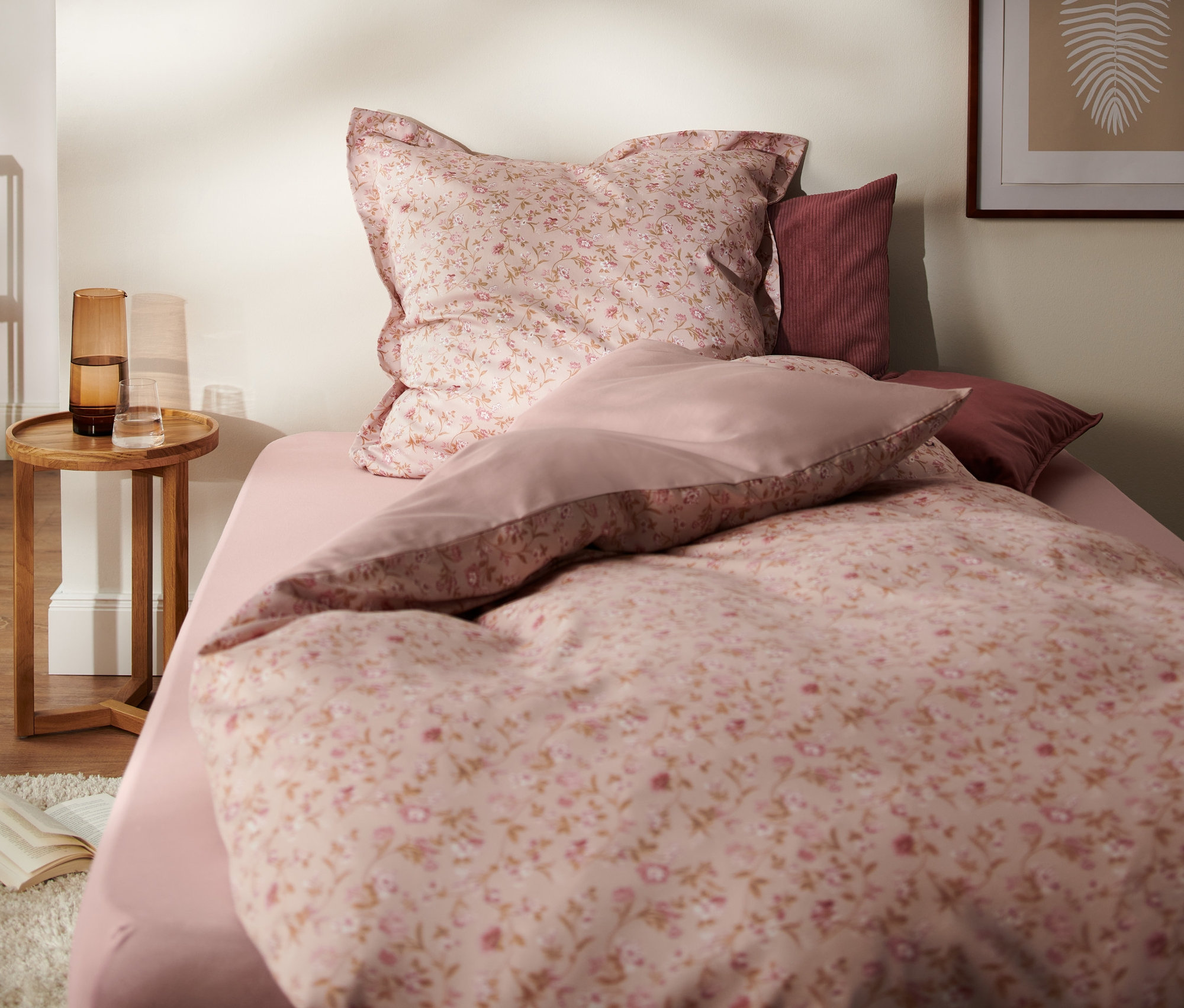 Schlafzimmer mit Bettwäsche-Set aus rosafarbenem Satin mit Blumenmuster, Nachttisch und Dekorationen. Im Bild sind eine Satin-Bettwäsche, Übergröße und eine Satin-Bettwäsche, Normalgröße zu sehen.