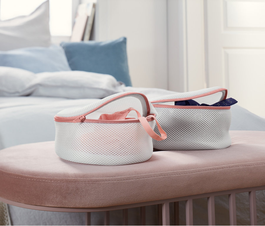 Zwei BH-Wäschenetze stehen auf einem rosa Hocker im Schlafzimmer.