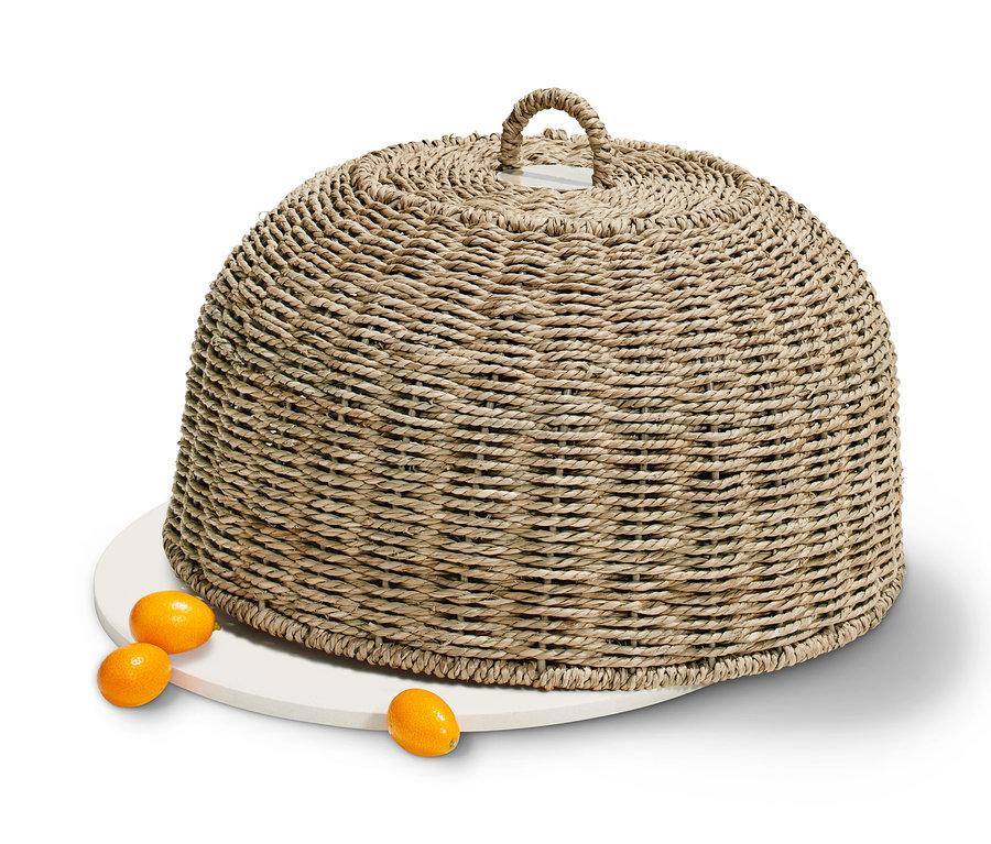 Eine Abdeckhaube aus Geflecht steht auf einem weißen Teller neben Kumquats.