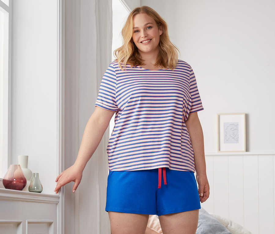 Frau steht im Schlafzimmer und trägt einen Shorty-Pyjama.