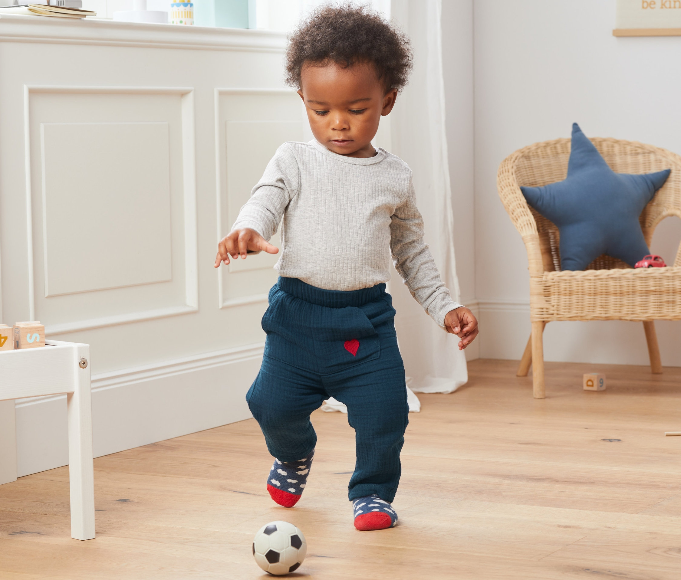 Kleiner Junge spielt mit einem Fußball und trägt eine blaue Schlupfhose aus Bio-Baumwolle.