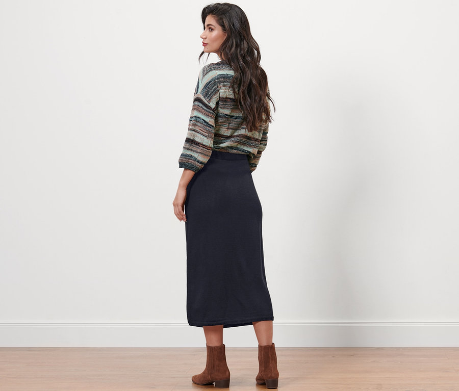 Frau steht mit dem Rücken zur Kamera und trägt einen dunkelblauen Strickrock.