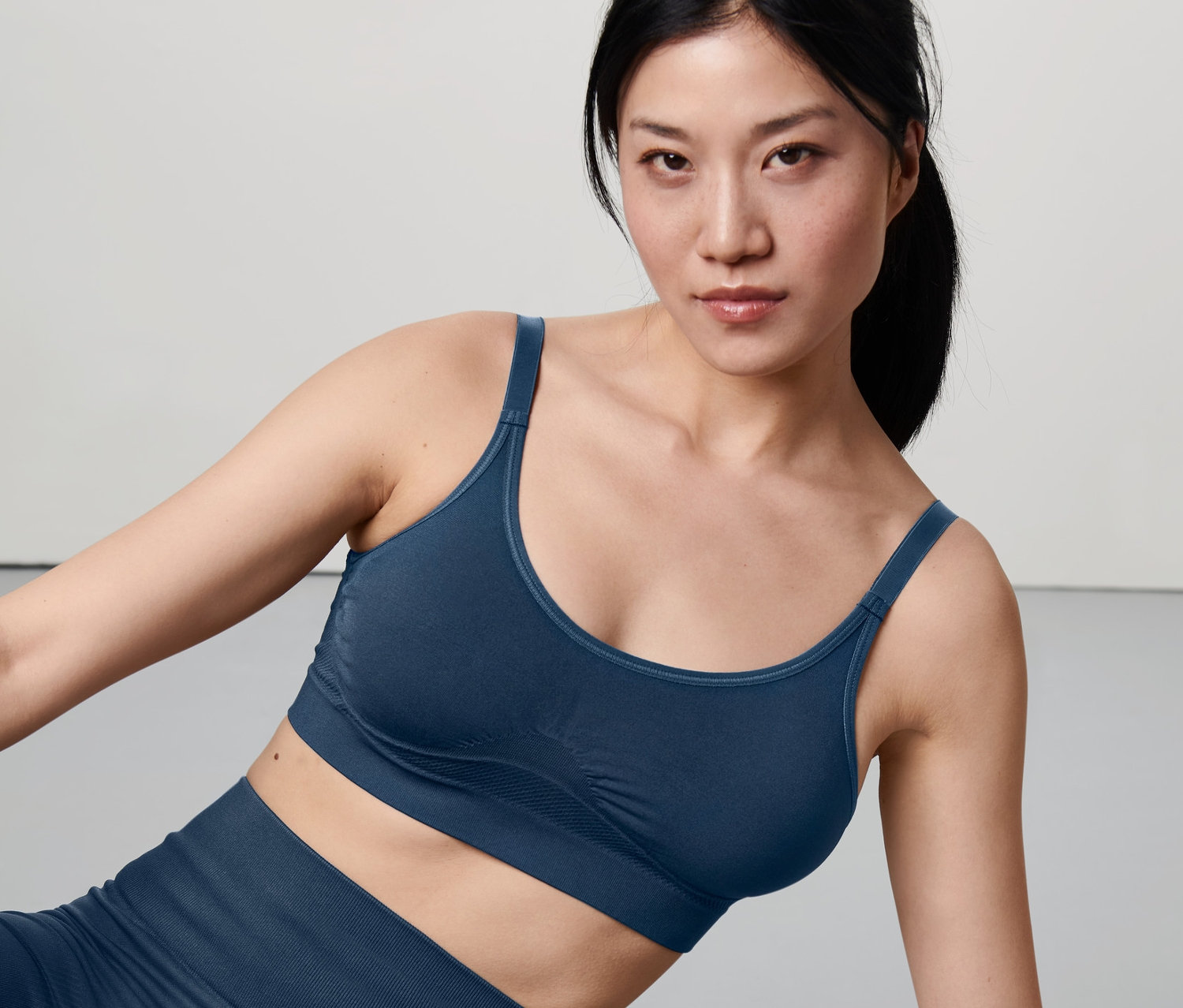 Asiatische Frau kniet und trägt einen dunkelblauen Seamless-Sport-BH und Leggings.