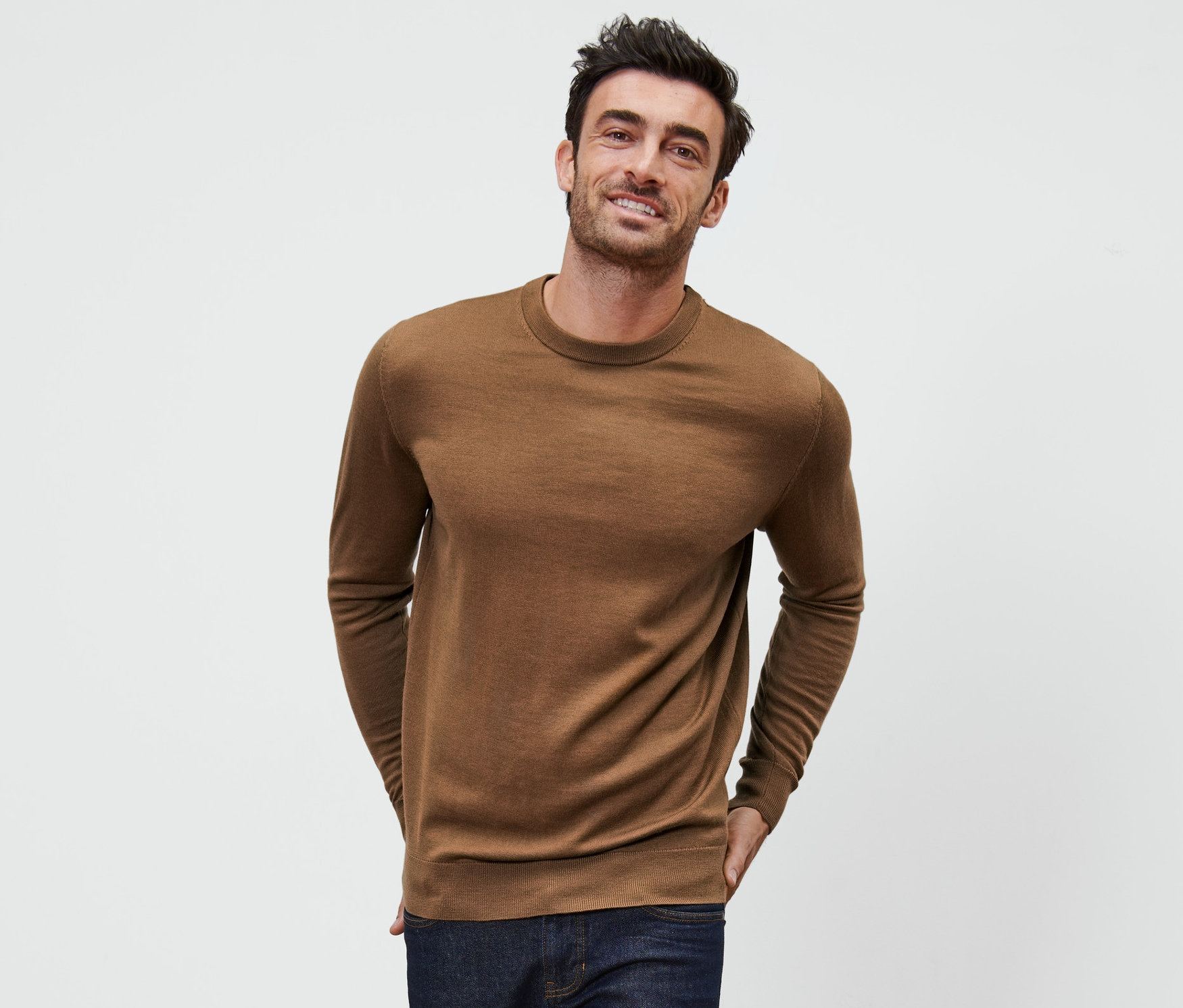 Mann posiert vor weissem Hintergrund mit einem cognacfarbenen Merino-Pullover.