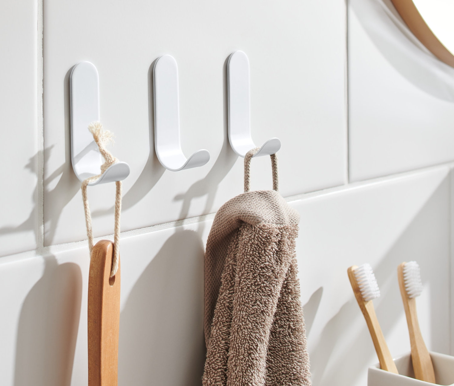 An weißen Fliesen hängen drei selbstklebende Haken, an denen eine Bürste und ein Handtuch hängen.