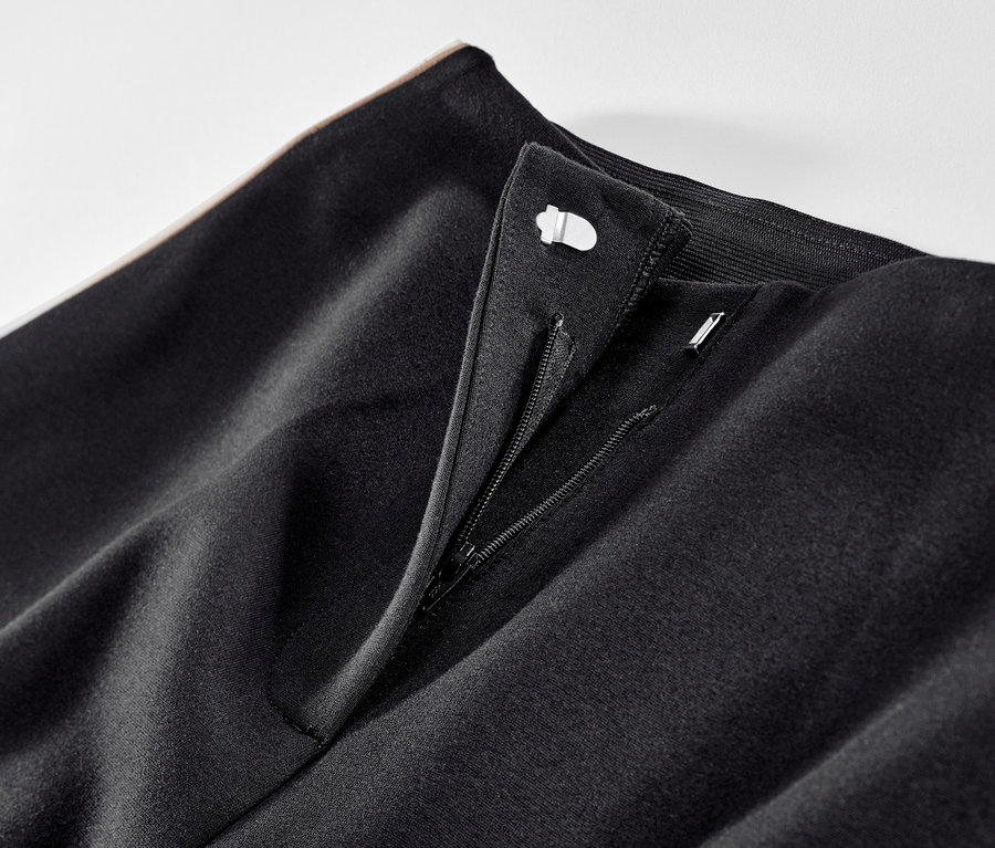 Detailaufnahme einer schwarzen Jerseyhose mit Galonstreifen und geöffnetem Reißverschluss.
