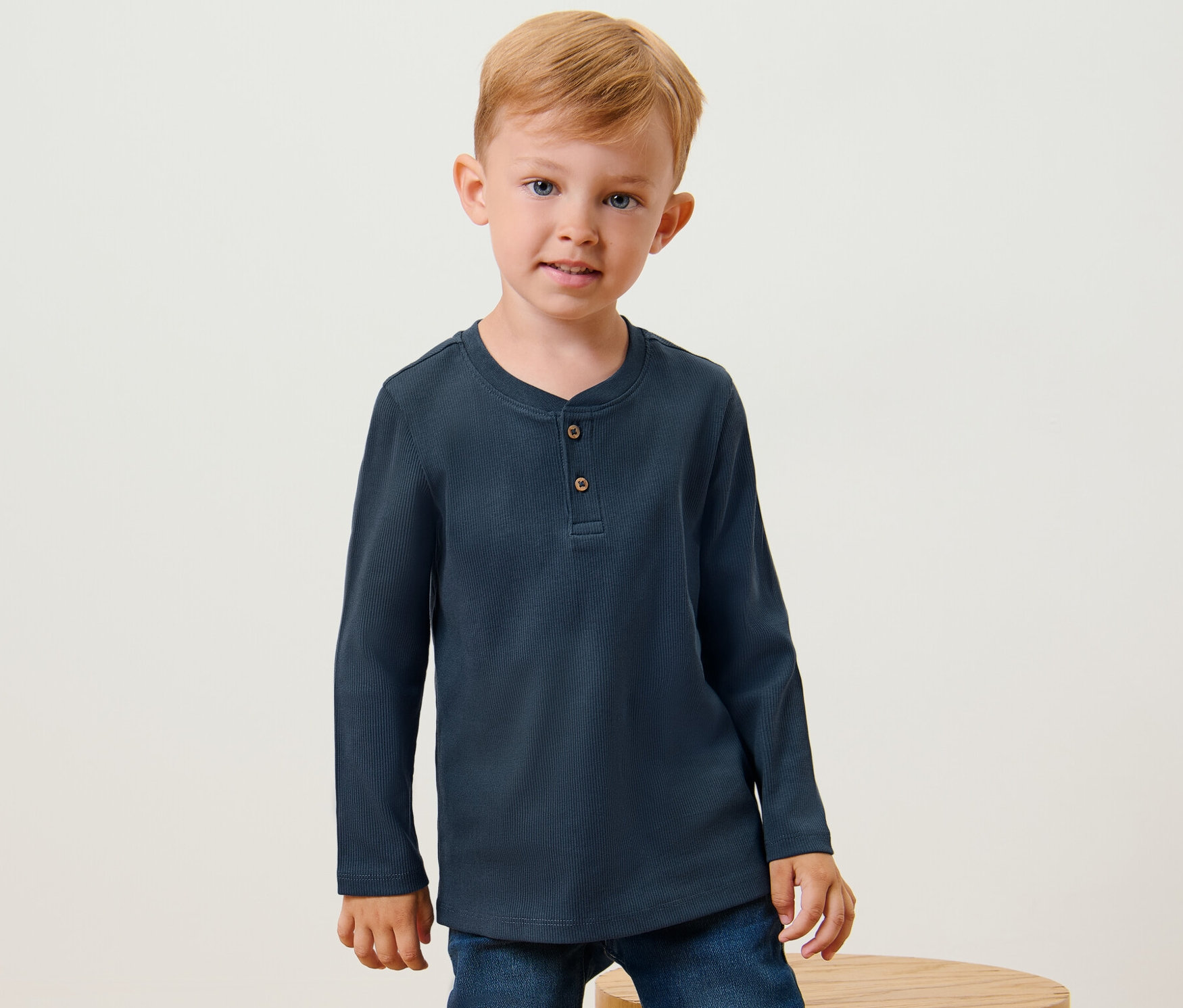 Ein Junge posiert in einem der 2 Kinder-Henley-Shirts mit Rippstruktur und Jeans.