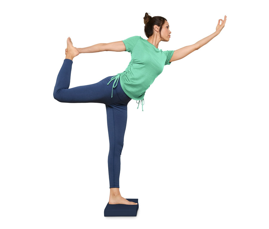 Frau im grünen Shirt balanciert in einer Tanzhaltung auf einem Balance-Pad.