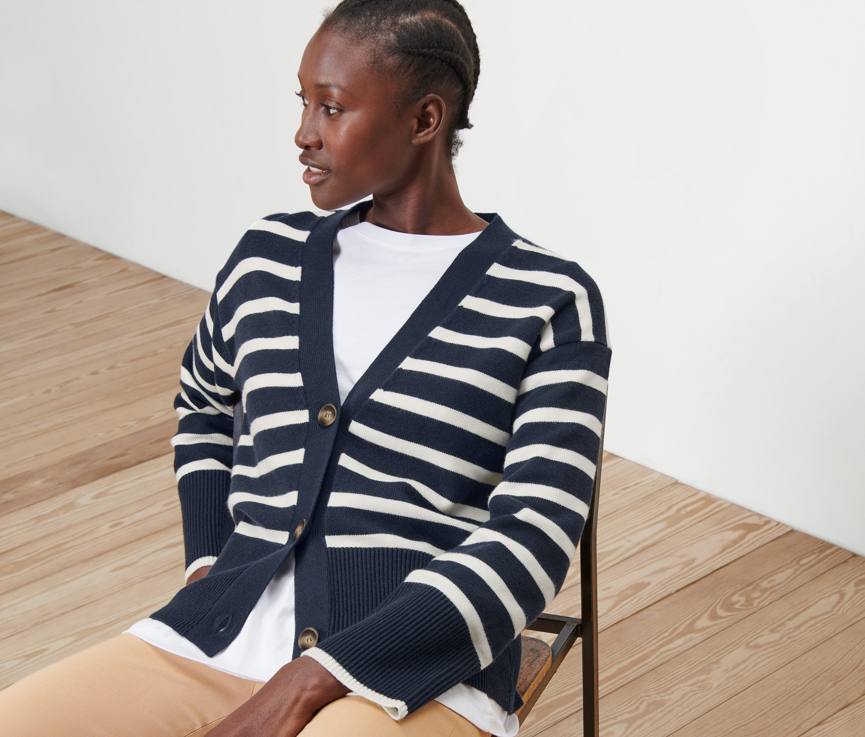 Frau sitzt auf Stuhl und trägt gestreiften Cardigan.
