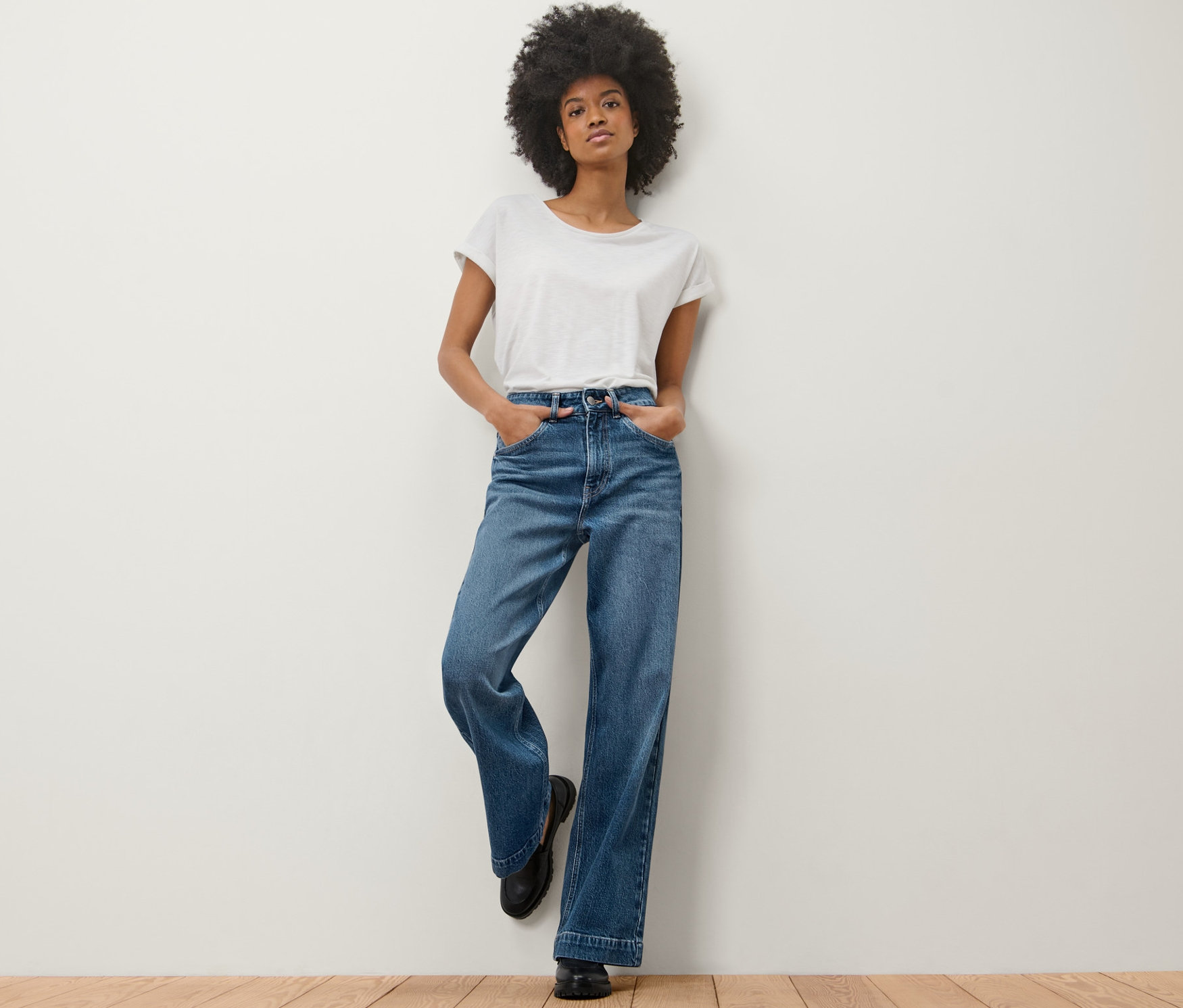 Eine Frau lehnt an einer Wand und trägt eine Wide Leg Jeans – Fit »Viki« und ein weißes T-Shirt.