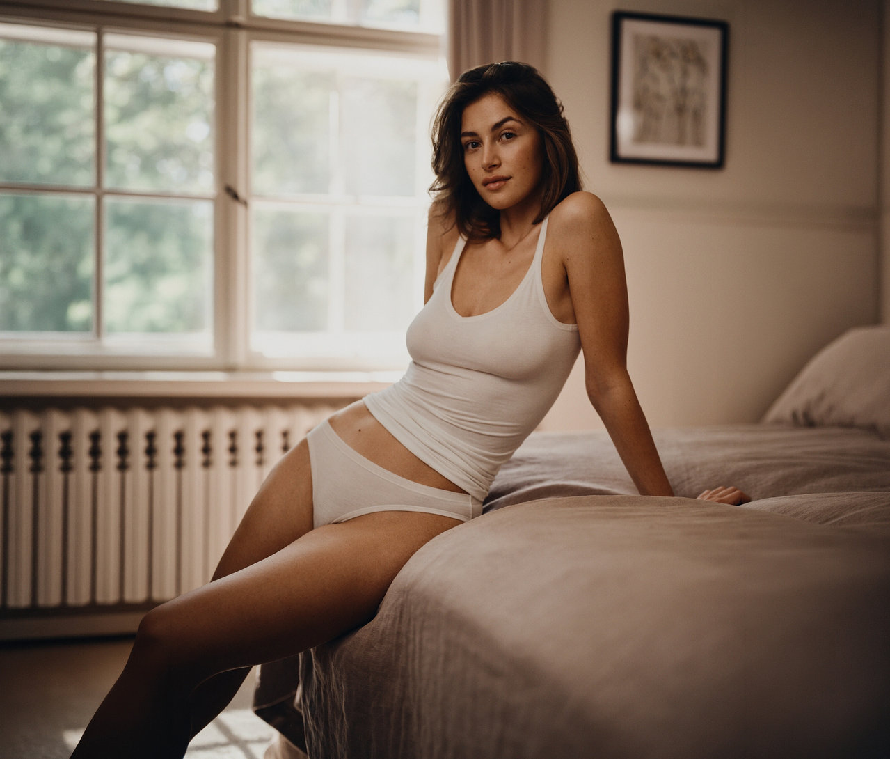 Frau sitzt im weißen 2 SCHIESSER Top auf einem Bett.