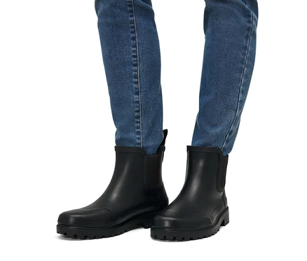 Beine in Jeans und Regenstiefeletten.
