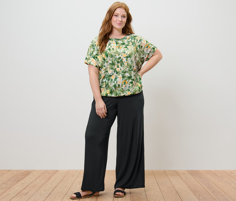 Eine Frau posiert in einem bedruckten Blusenshirt und einer Palazzohose.