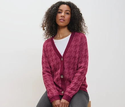 Frau sitzt und trägt einen Grobstrick-Cardigan mit Hahnentritt-Jacquard.