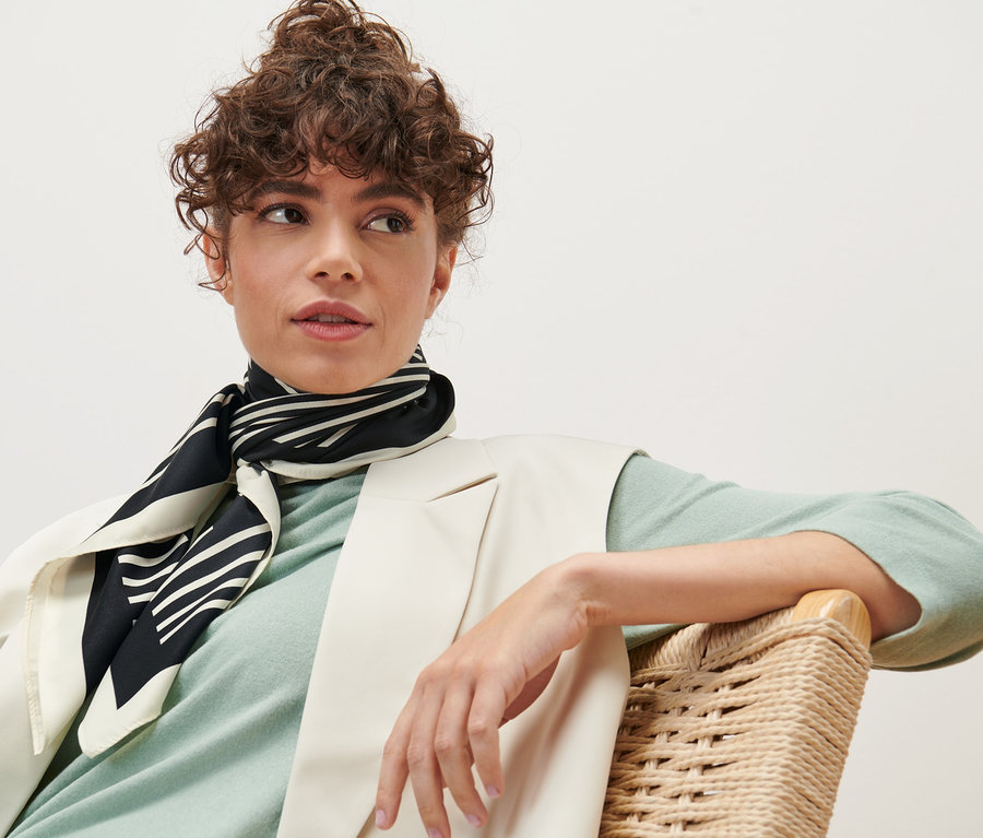 Frau sitzt im Sessel und trägt ein Halstuch.