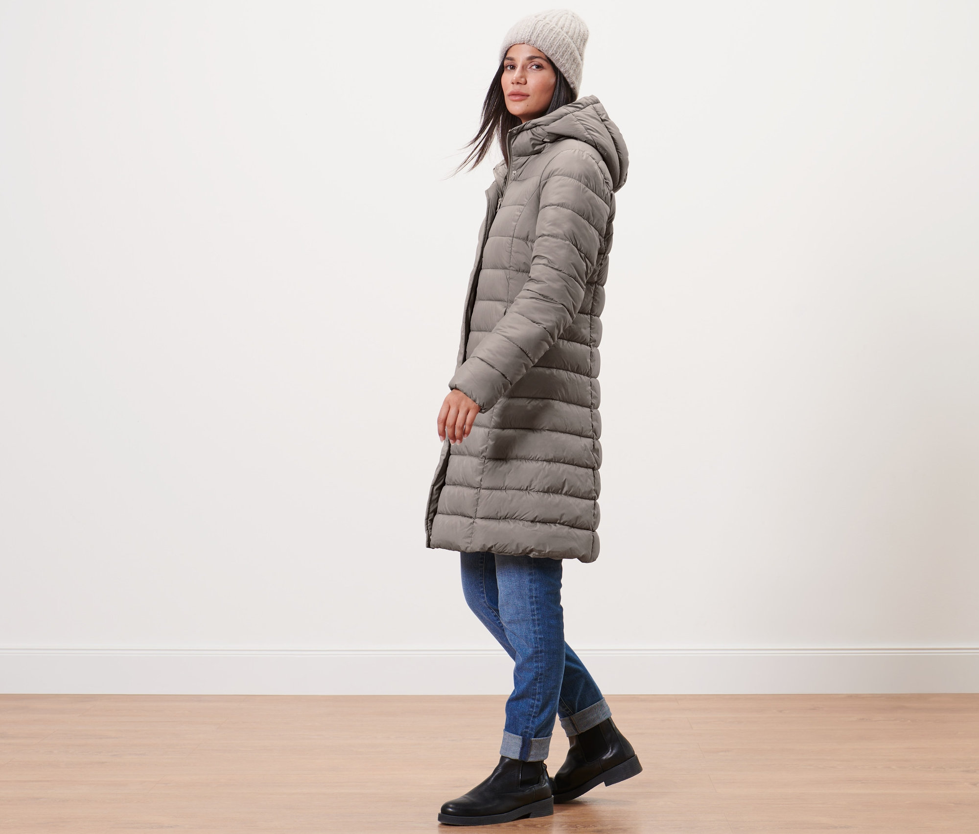Frau posiert seitlich in Steppmantel mit Kapuze, taupefarben, dazu Jeans und schwarze Schuhe.