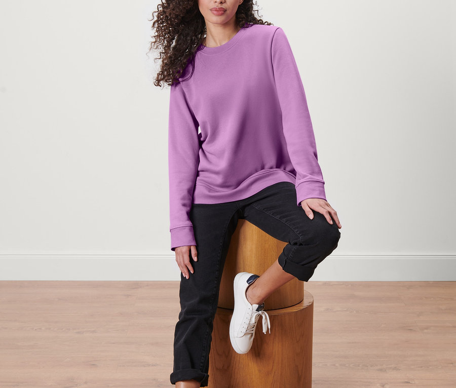 Frau sitzt auf einem Holzhocker und trägt ein Sweatshirt.