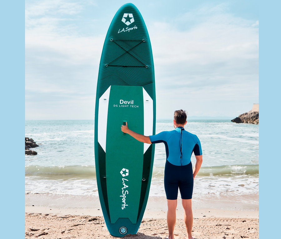 Mann steht am Strand neben dem grünen SUP-Board »Devil«.