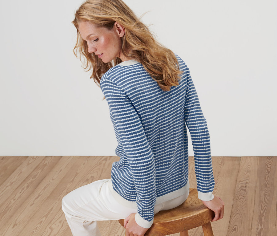 Frau sitzt auf einem Holzhocker und trägt einen gestreiften Feinstrickpullover.