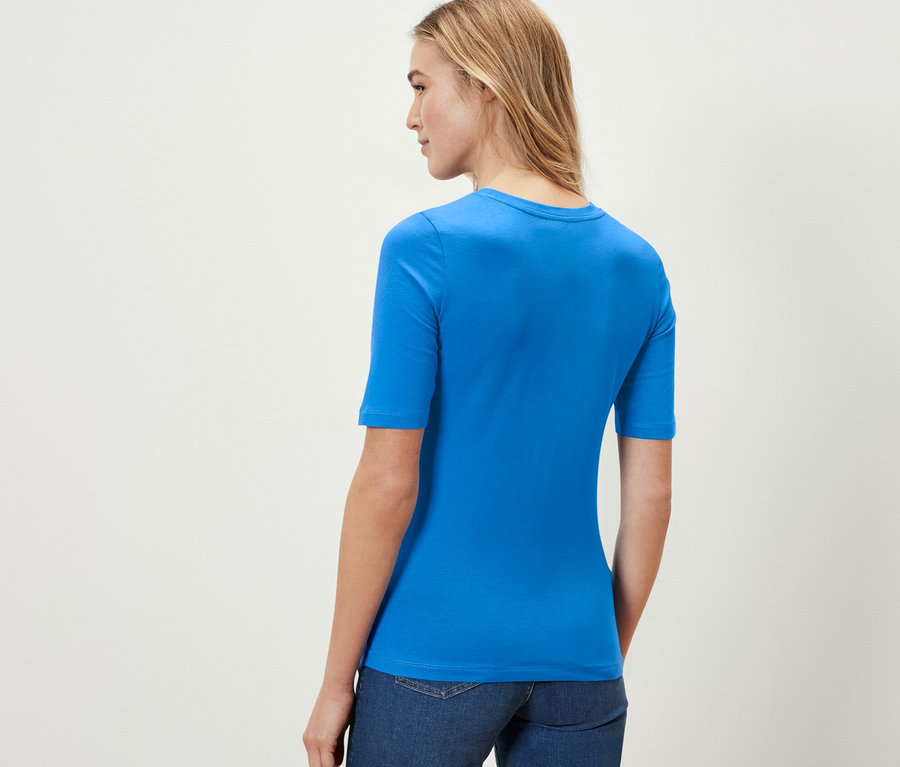 Frau trägt ein kobaltblaues Halbarmshirt und Jeans.