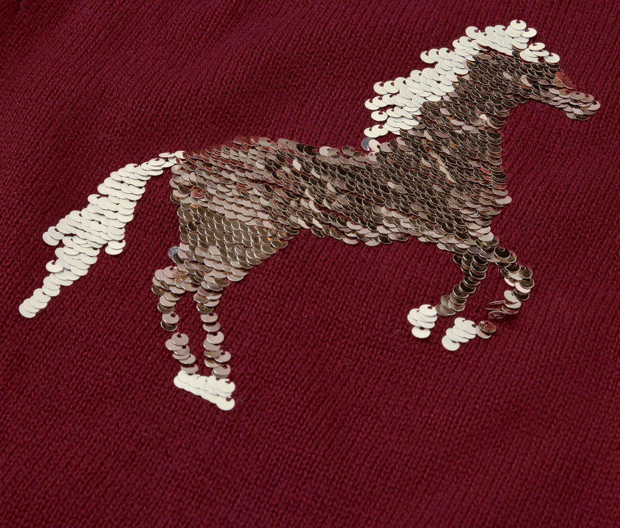 Detailaufnahme eines Kinder-Strickpullovers mit einem mit Pailletten verzierten Pferdemotiv.