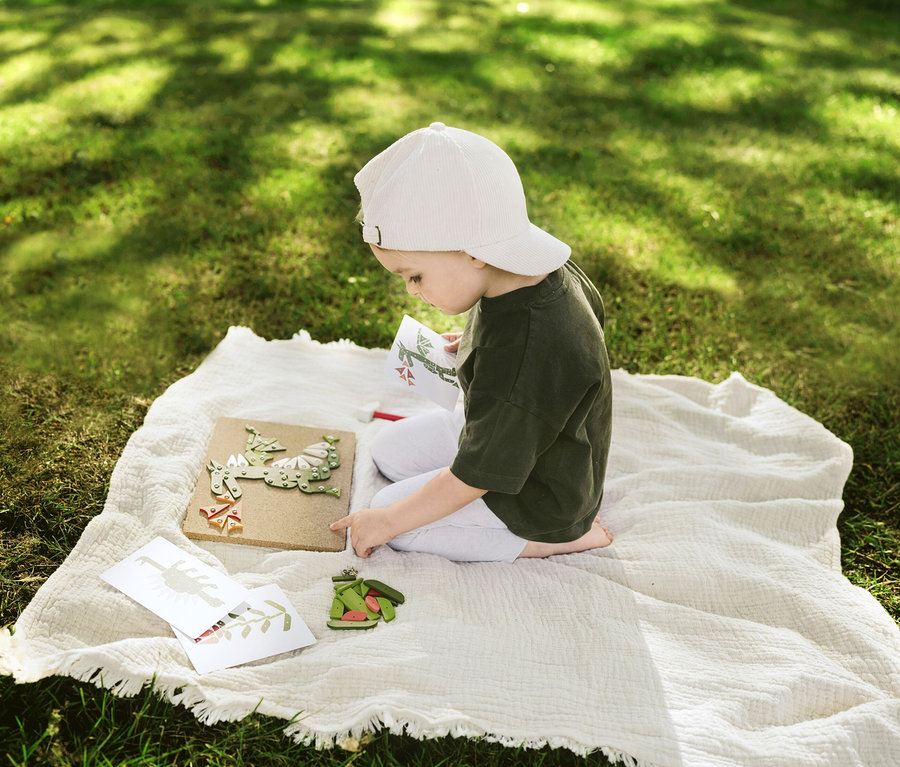 Kind spielt mit small foot Hämmerchenspiel, Pflanzen und Lebewesen auf einer Decke im Gras.