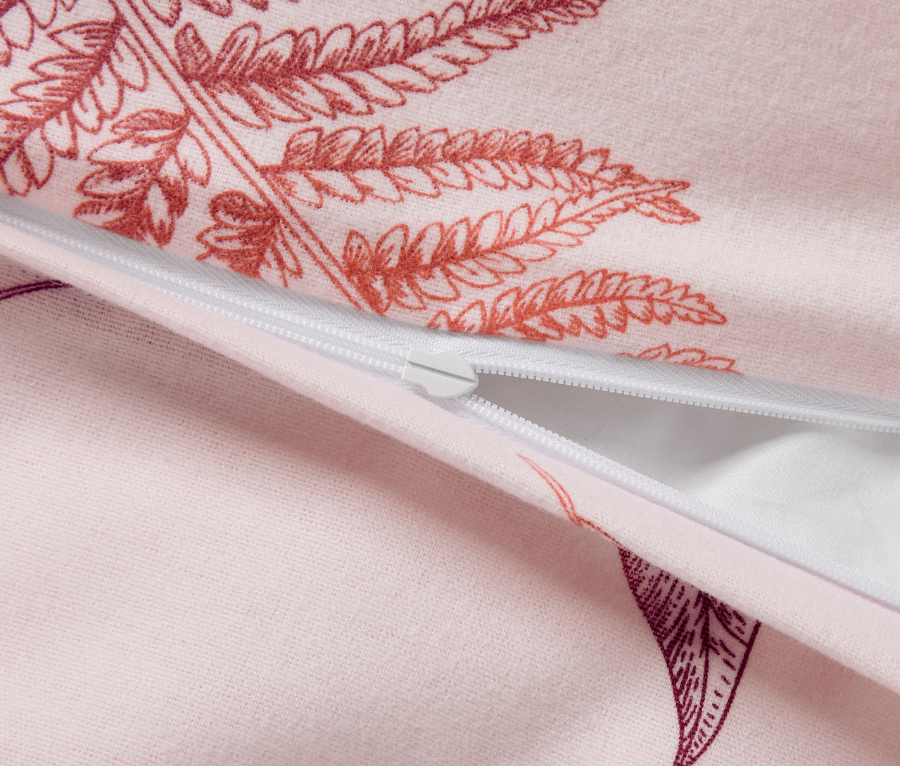 Detailaufnahme eines rosa Bettbezugs mit Farnmuster und weißem Reißverschluss.