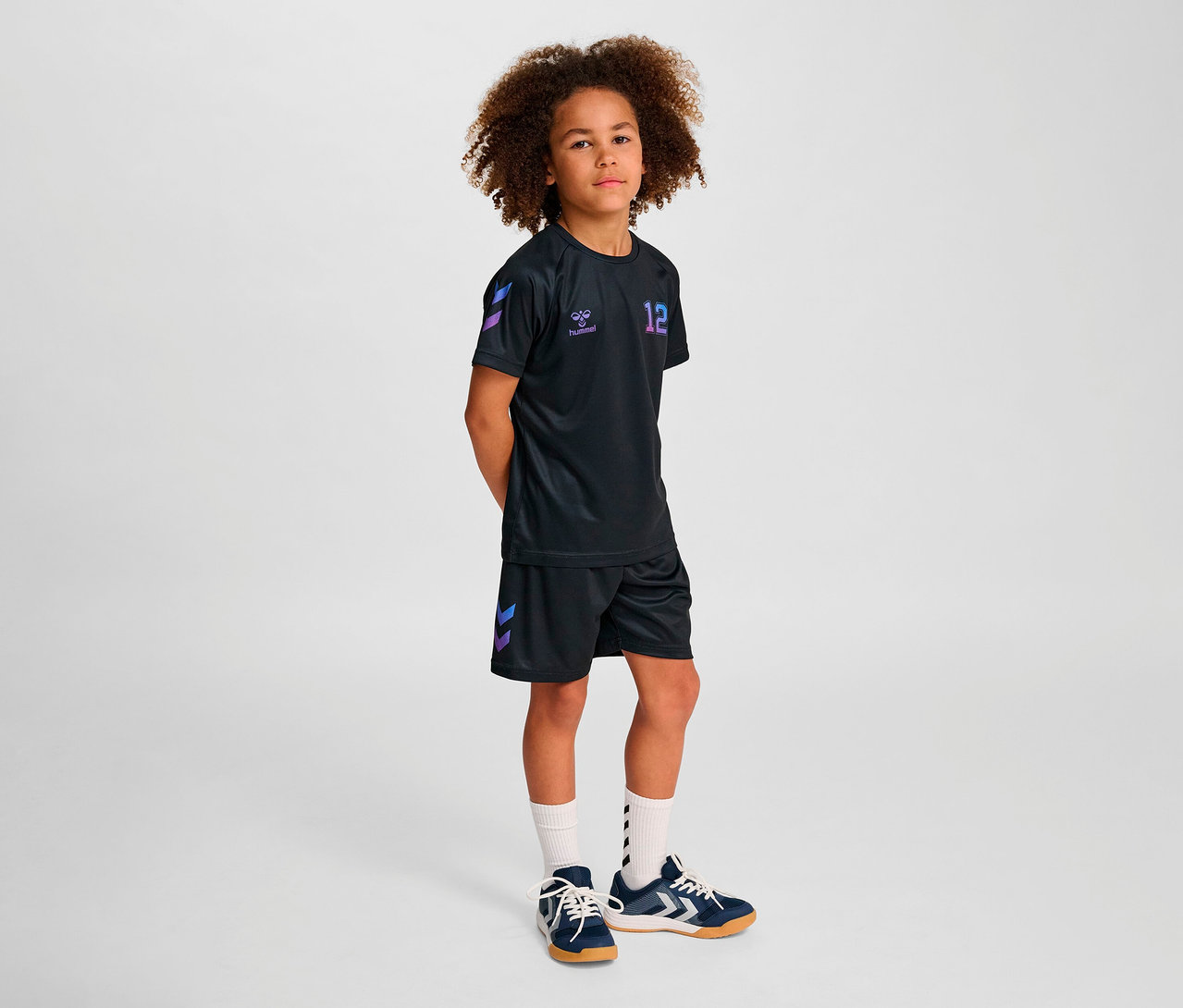 Junge, der vor hellem Hintergrund steht, trägt ein HUMMEL HMLJR Shimmer T-Shirt S/S Set.